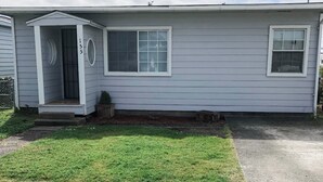 Une maison de plain-pied avec un porche à l’avant, une porte de garage et un petit jardin devant.