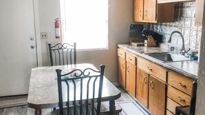 Une cuisine de taille réduite, dotée de meubles en bois, d’un plan de travail en marbre et d’une table à manger avec des chaises.