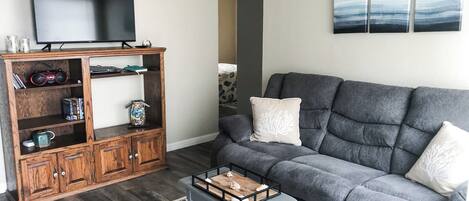 A living room with a grey sofa, a wooden entertainment unit, and a flat-screen TV.