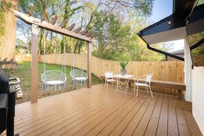 A wooden deck with a pergola, white outdoor furniture, and a barbecue grill.
