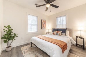 A bedroom with a bed, two bedside tables, a ceiling fan, and a potted plant.