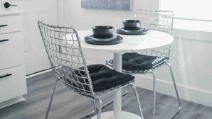 A modern dining area with a round table and wireframe chairs, a white cabinet, and a window with a view. - Modern Uptown Getaway & Backyard Oasis (Charlotte)