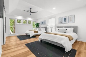 Two single beds and a larger bed with a grey headboard, set against a backdrop of framed artwork and natural light.