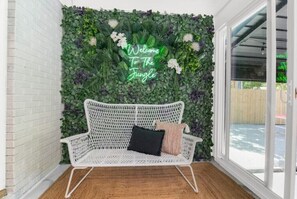 Sit comfortably on the wicker bench amidst lush greenery and a vibrant welcome sign.