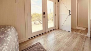 A bedroom with a large sliding door leading to a balcony, a bed with a floral bedspread, and a wooden floor. - The Lakehouse at Canyon Lake (Canyon Lake)