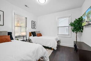 A bedroom with two single beds, a small table, a plant, and a TV on the wall. - Walkable Uptown Boho Retreat (Charlotte)