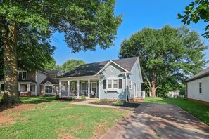 A two-story house with a porch, surrounded by trees and a well-maintained lawn. - Walkable Uptown Boho Retreat (Charlotte)