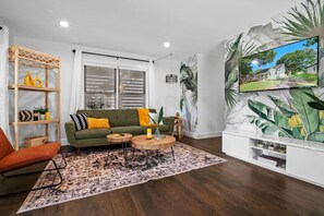A living room with a green sofa, wooden side table, and a patterned rug. - Walkable Uptown Boho Retreat (Charlotte)