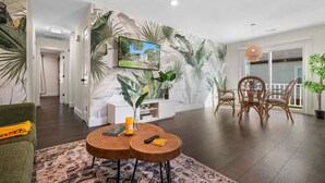 Un salon moderne agrémenté d’une grande fresque murale, d’un téléviseur et d’un coin repas avec des chaises en osier.