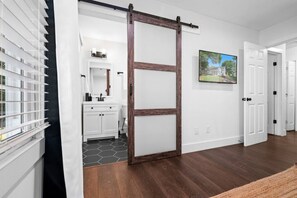 A hallway with a sliding barn door, a white bathroom with a hexagonal tile floor, and a painting on the wall. - Walkable Uptown Boho Retreat (Charlotte)