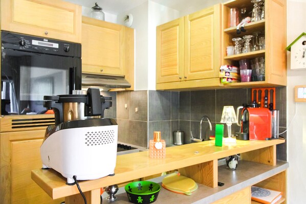 A kitchen with wooden cabinets, a black oven, a white food processor, and various kitchen items on the counter. - Beautiful 2-bed Family Apartment, Flaine Montsoleil (Flaine)