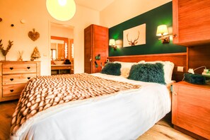 A hotel room with a large bed, wooden headboard, a green accent wall, a mirror, a wooden dresser, and a nightstand with a lamp. - Beautiful 2-bed Family Apartment, Flaine Montsoleil (Flaine)