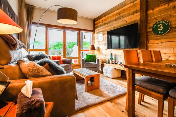 Ein gemütliches Wohnzimmer mit einer Couch, Sesseln, einem Couchtisch und einem Fernseher.