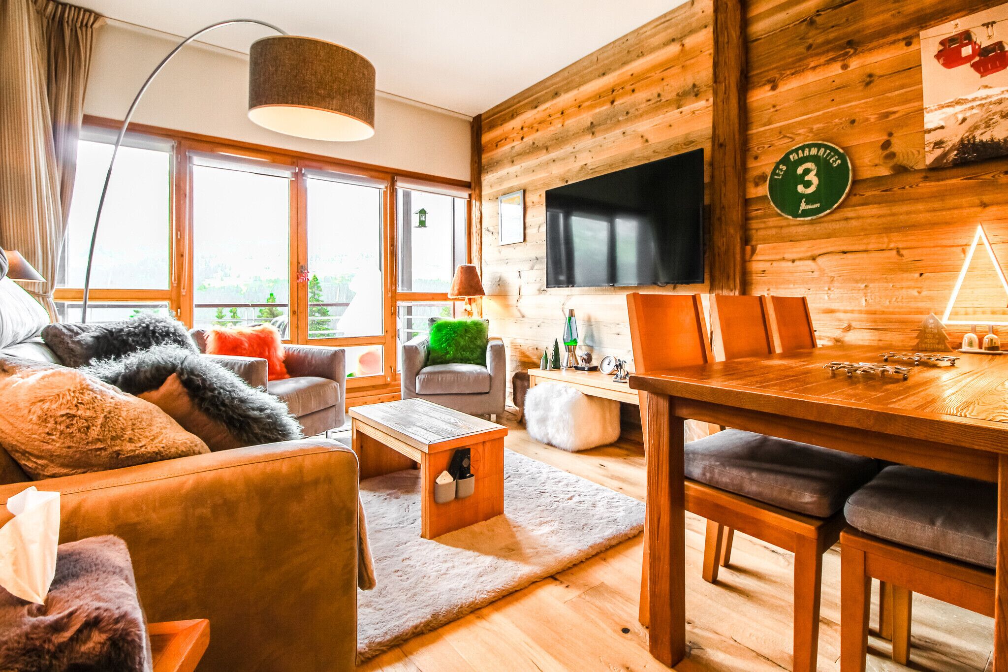 Una sala de estar acogedora con pared de madera, televisor, mesa de comedor y un sofá con cojines suaves.