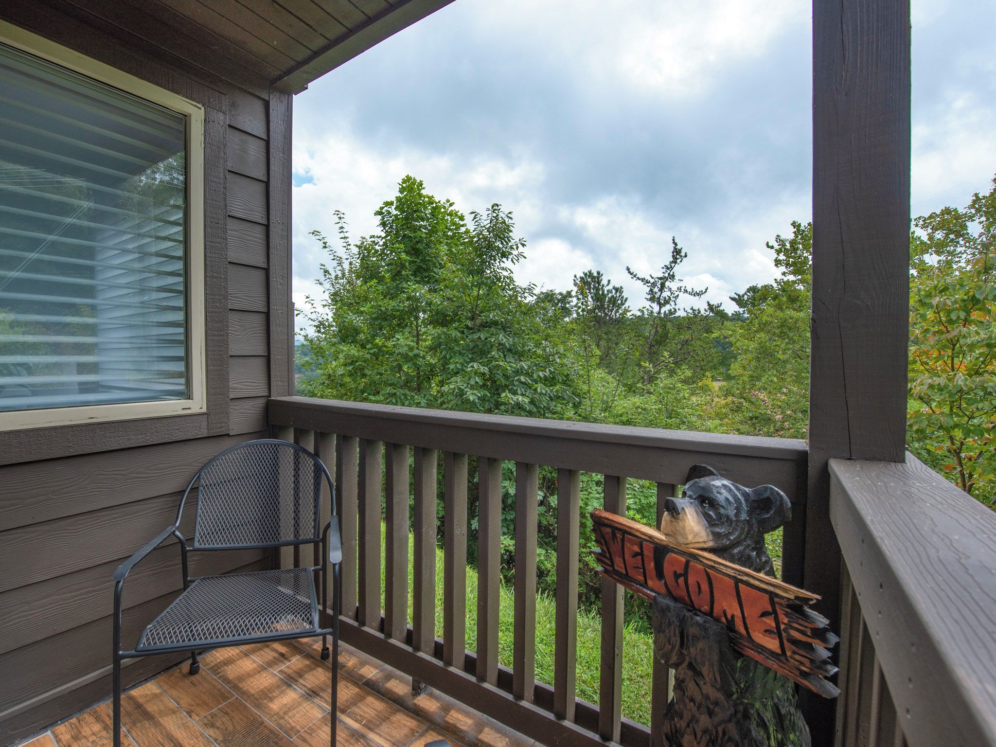 A wooden deck with a metal chair and a bear sculpture with a 'Welcome' sign.