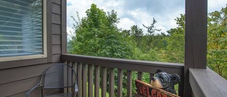 A wooden deck with a metal chair and a bear sculpture with a 'Welcome' sign.