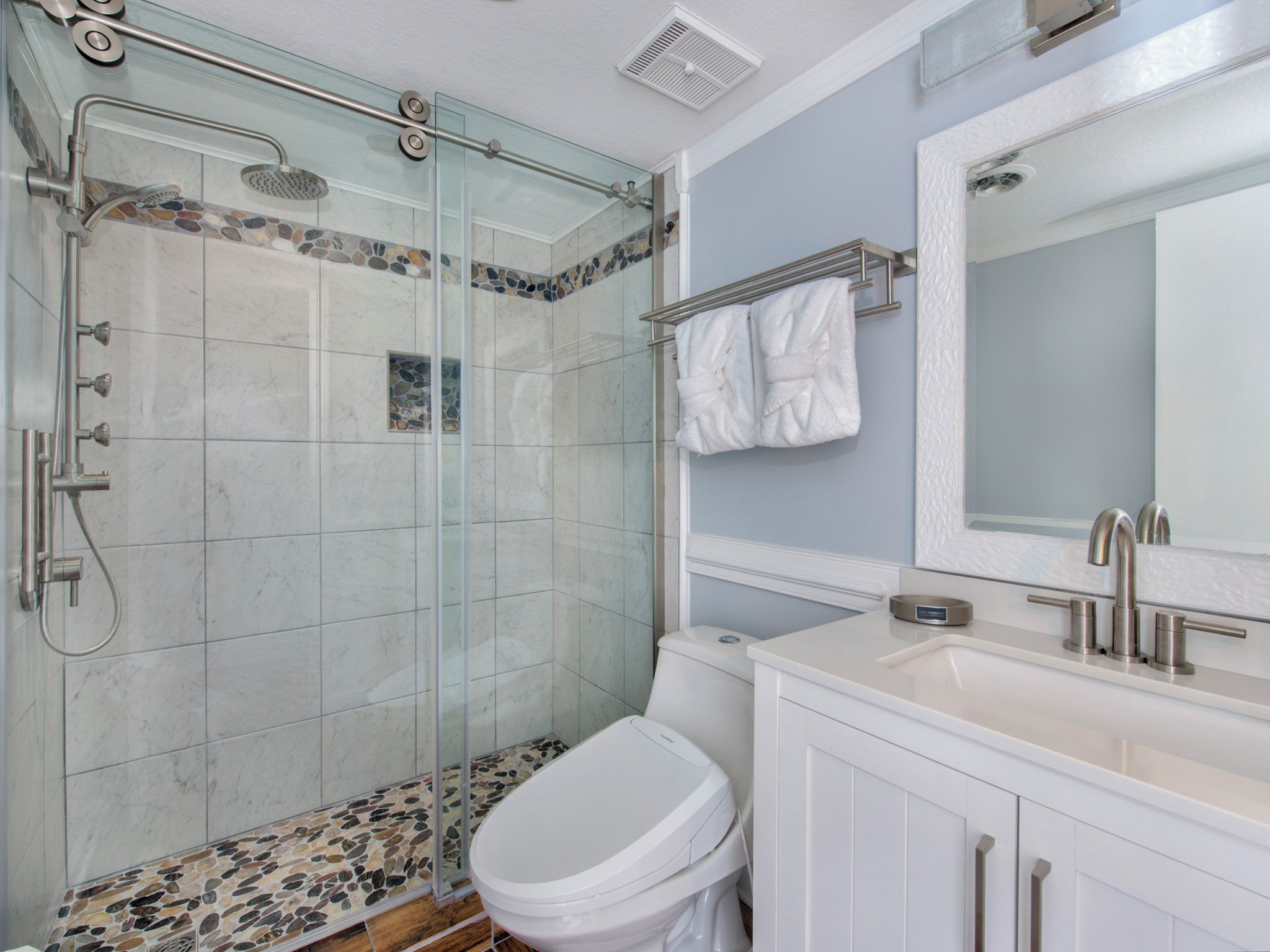 Un baño con cabina de ducha de vidrio, inodoro blanco y lavamanos con espejo.