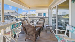 A covered outdoor area with wicker furniture, a ceiling fan, and a view of neighboring houses. - Celestial Dreams by Ryson Vacation Rentals (Galveston)