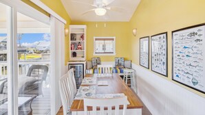 A dining area with a wooden table, white chairs, and a ceiling fan. - Celestial Dreams by Ryson Vacation Rentals (Galveston)