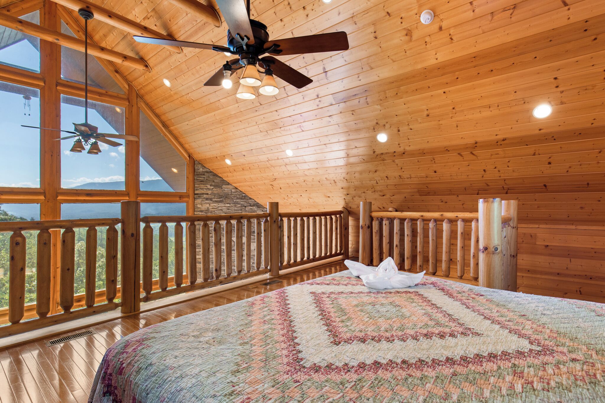 Une pièce spacieuse avec un grand lit, un ventilateur de plafond et une vue sur l’extérieur grâce à de grandes fenêtres.
