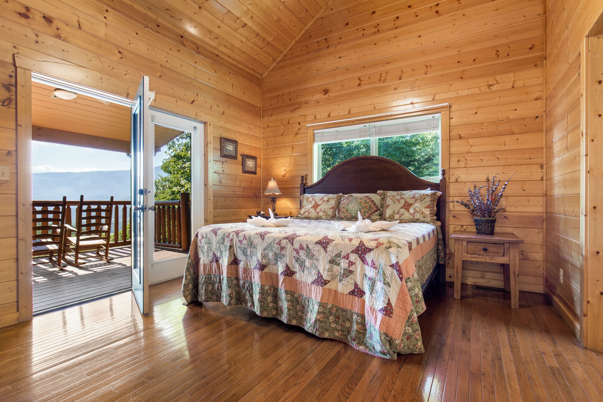 Un dormitorio de cabaña de madera con una cama, una mesita de noche, una ventana y una puerta que da a una terraza exterior.