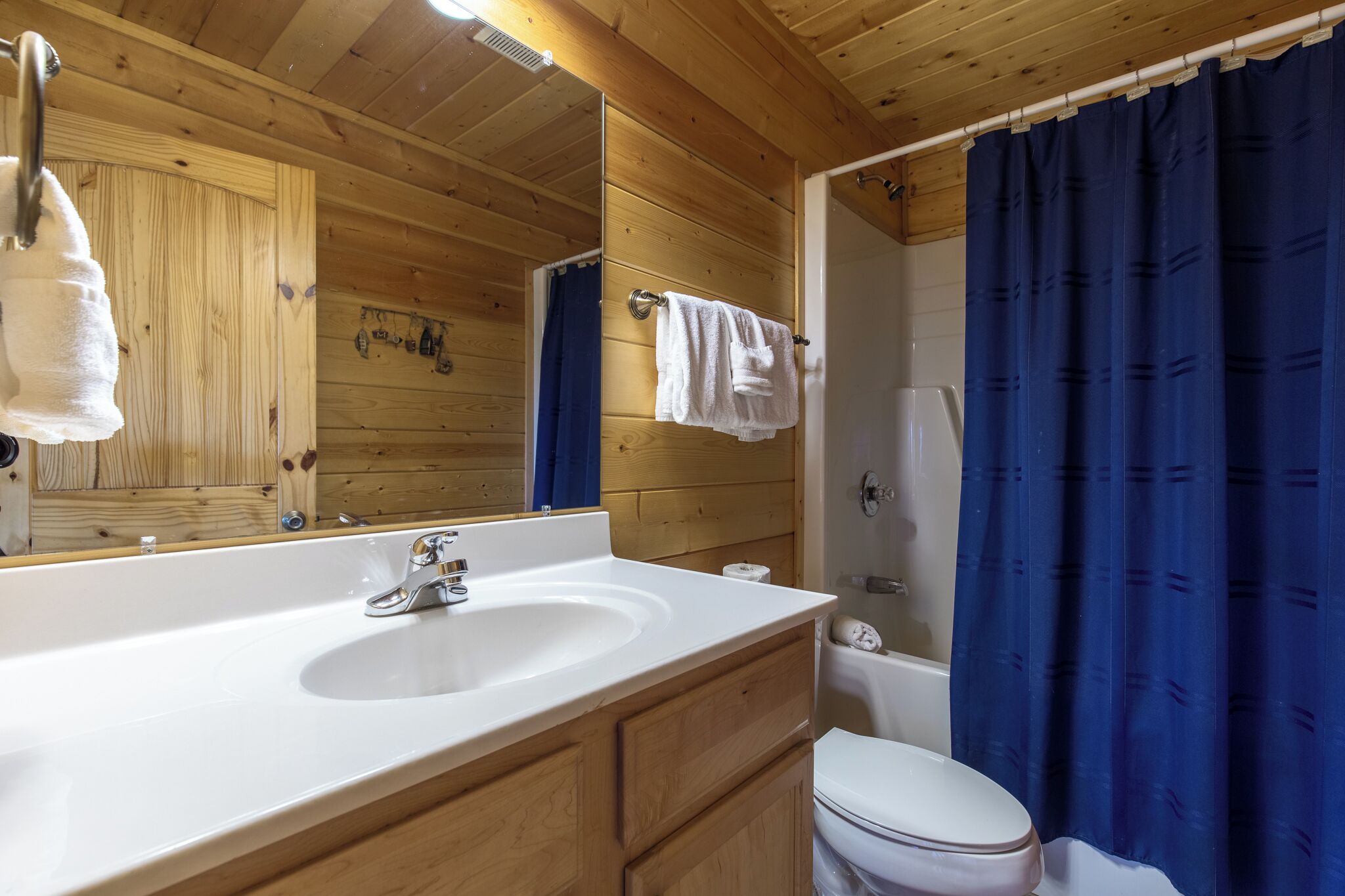 A wooden cabin bathroom with a white sink, a mirror, a towel rack, a shower curtain, and a toilet.