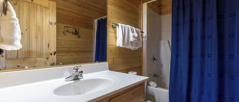 A wooden cabin bathroom with a white sink, a mirror, a towel rack, a shower curtain, and a toilet.