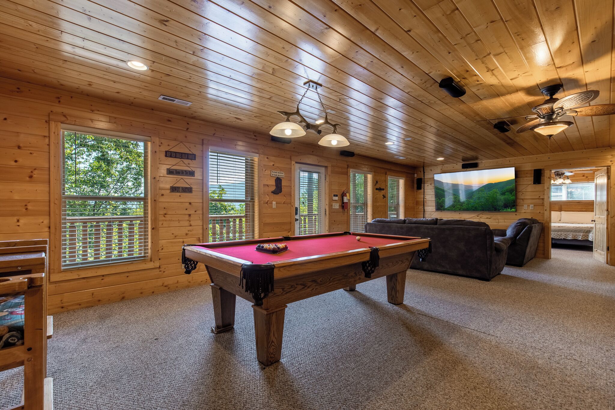 A wooden interior with a pool table, seating area, and large windows.
