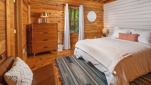 Une chambre dans une cabane en bois, avec un lit, une commode et une fenêtre avec des rideaux.