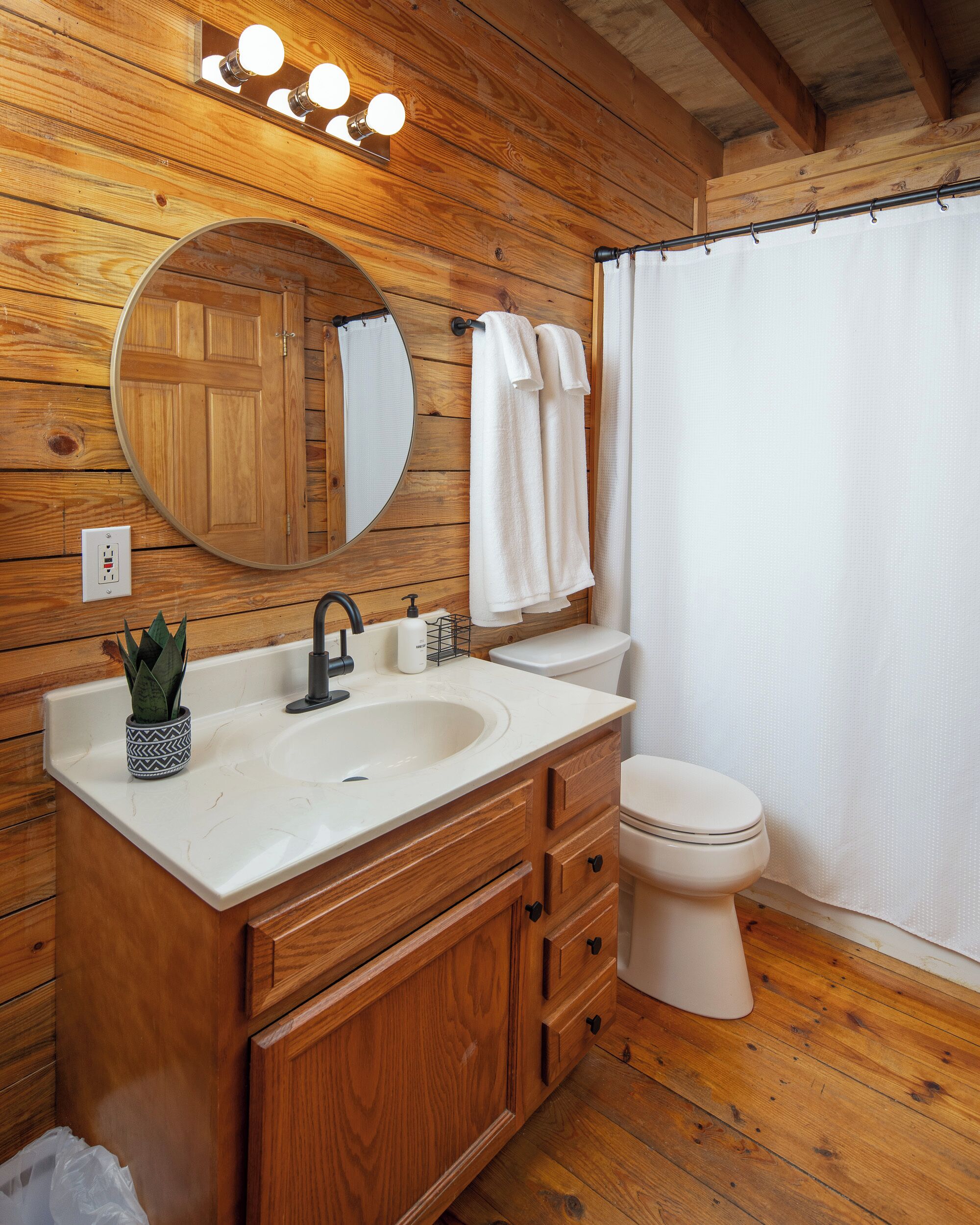 A wooden bathroom with a sink, mirror, and toilet.