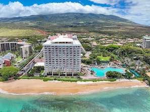 A hotel with a pool, beachfront, and mountainous background.