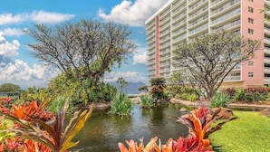 Un hotel con un edificio grande, un estanque y plantas tropicales.