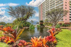 A hotel with a large building, a pond, and tropical plants.