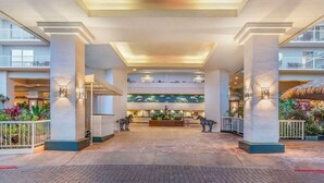 Un vestíbulo espacioso con un mostrador de recepción central, varios pisos visibles y una exhibición de plantas tropicales.