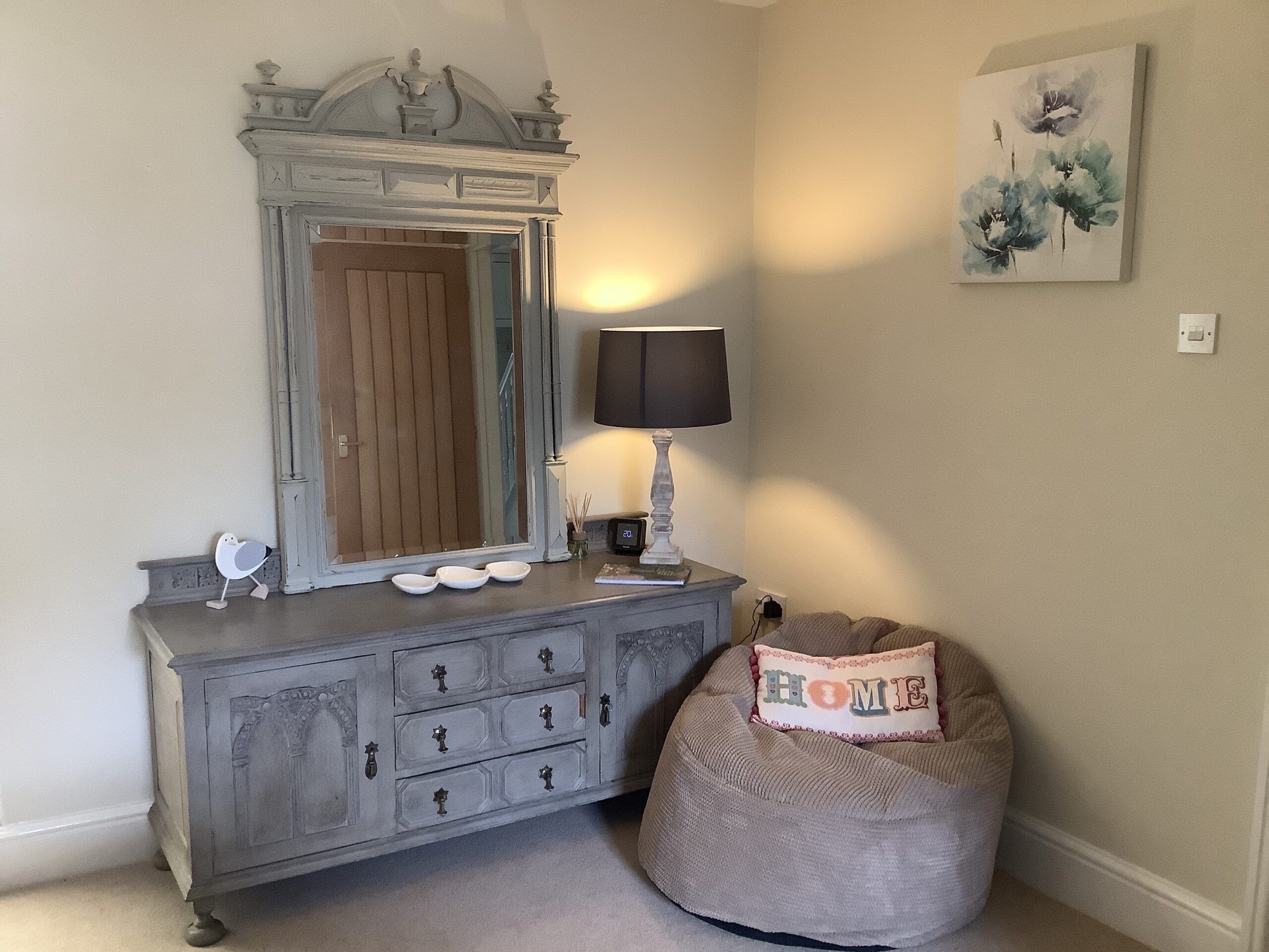 Une pièce comprenant une commode ancienne, une lampe, un fauteuil en forme de sac et un tableau accroché au mur.