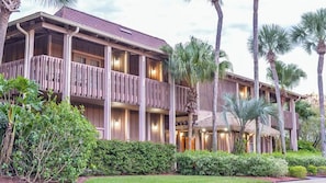 A multi-story hotel with balconies, palm trees, and a well-maintained garden.