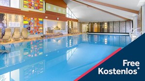Une grande piscine intérieure à l’eau d’un bleu cristallin, dotée d’une verrière et d’un aménagement intérieur moderne.