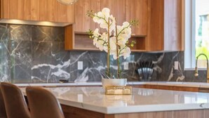 A modern kitchen with marble countertops, wooden cabinets, and a central island with chairs.