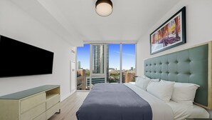 Une chambre moderne avec un grand lit, un téléviseur à écran plat, une tête de lit verte et une vue sur la ville.