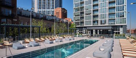 A rooftop pool with lounge chairs and a modern building in the background.