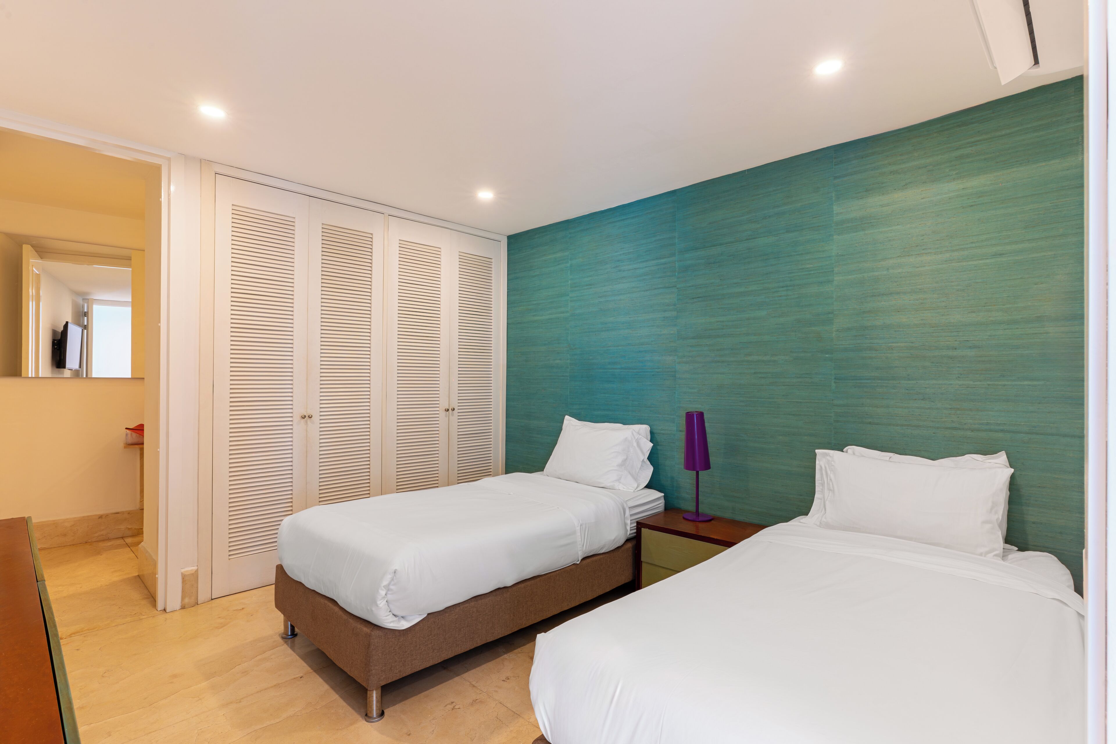A hotel room with two beds, a wardrobe, a nightstand, and a lamp.