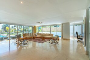 A spacious living room with a large sectional sofa, a coffee table, and a view of a pool through large windows.