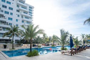 A swimming pool with lounge chairs and palm trees, surrounded by a modern building. - Wynwood Morros Epic in Cartagena (Cartagena)