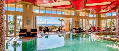 Una piscina interior con agua cristalina, rodeada de sillones de descanso y vistas al océano.