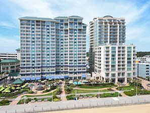 Three interconnected buildings offer a grid-like facade and balconies, surrounding a landscaped courtyard with pathways, seating areas, and a pool.