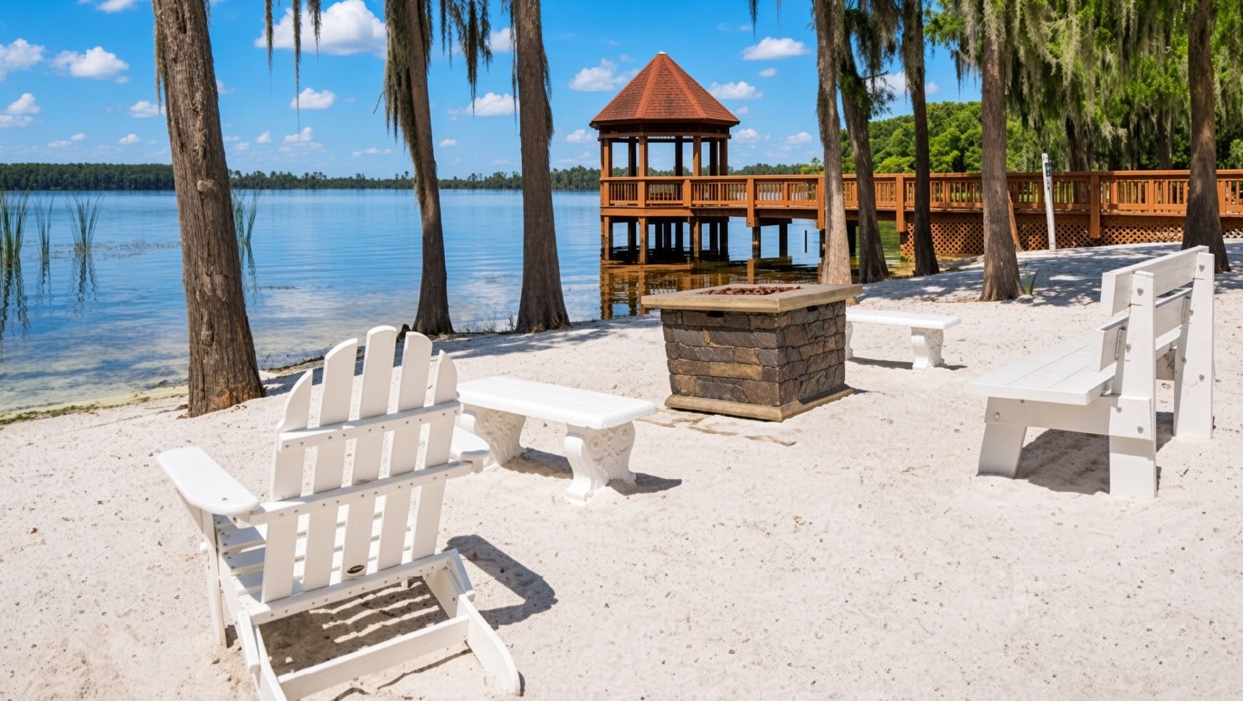 Una playa con sillas Adirondack blancas, un hogar de piedra y un pabellón de madera.