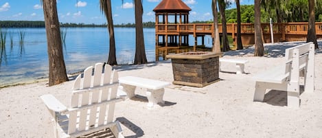 Una playa con sillas Adirondack blancas, un hogar de piedra y un pabellón de madera.