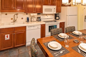 A kitchen with wooden cabinets, a microwave, a stove, a dishwasher, and a dining table set for two with plates, glasses, and cutlery. - Orlando | Crew Lake Hub | Pool + Hot Tub | 3BR Sleeps 8 (Orlando)