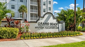 Señal del Grand Beach Hilton Vacation Club con un jardín ajardinado en primer plano.