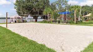 Una cancha de voleibol de playa con arena, una red, rodeada de vegetación y un lago.
